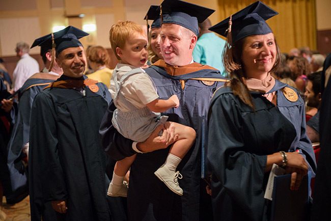 graduates walking in line, one holding a baby