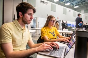 Two WVU students sitting at laptops in a large room